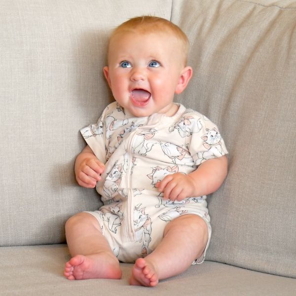 A baby propped up in the corner of a couch, looking up with a big smile