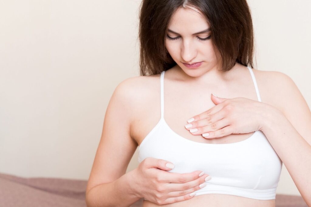 Woman with mastitis in a white crop top lightly touching her tender breast