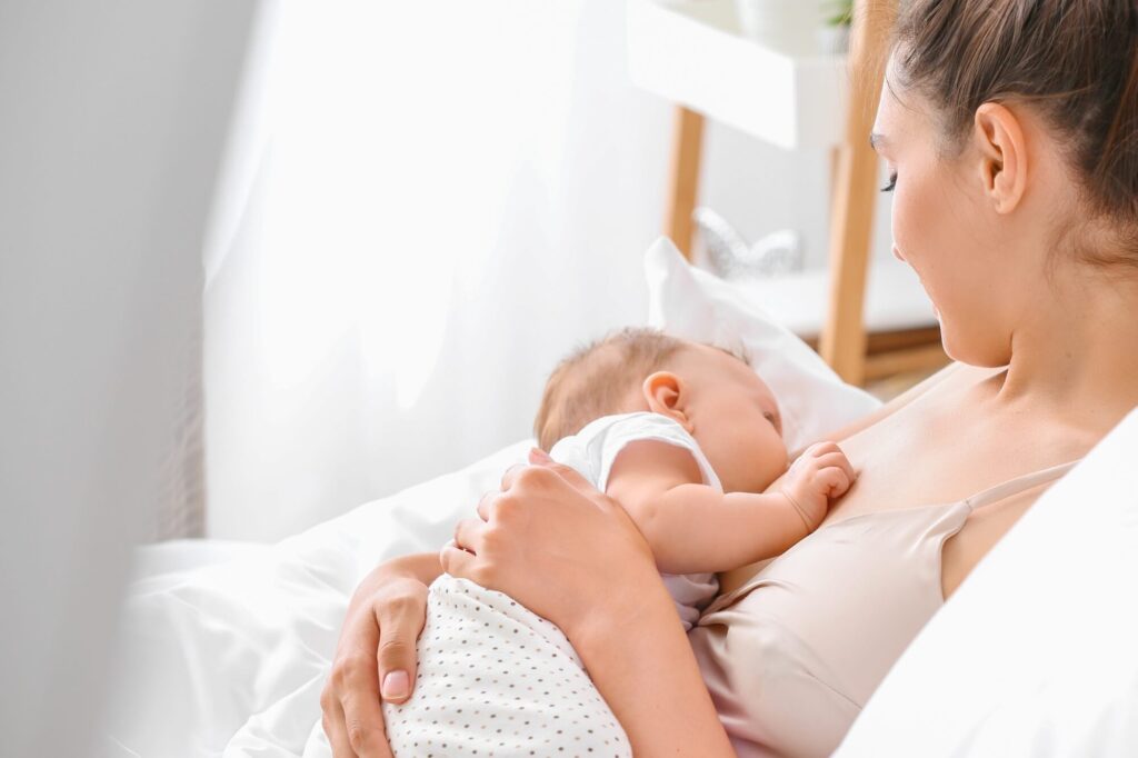 Mother looking down breastfeeding her baby on a bed with white sheets
