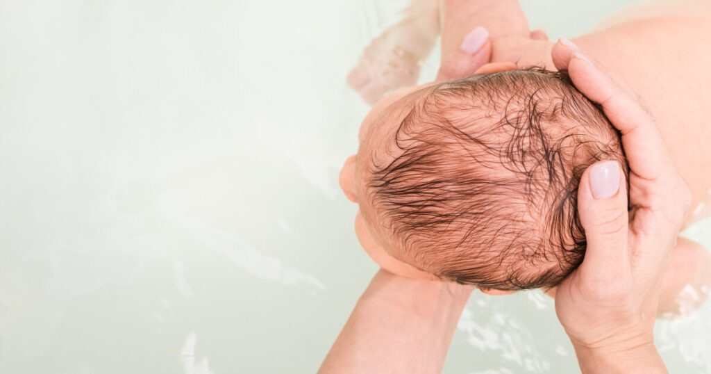 Newborn baby having a bath on its tummy supported by mothers hands